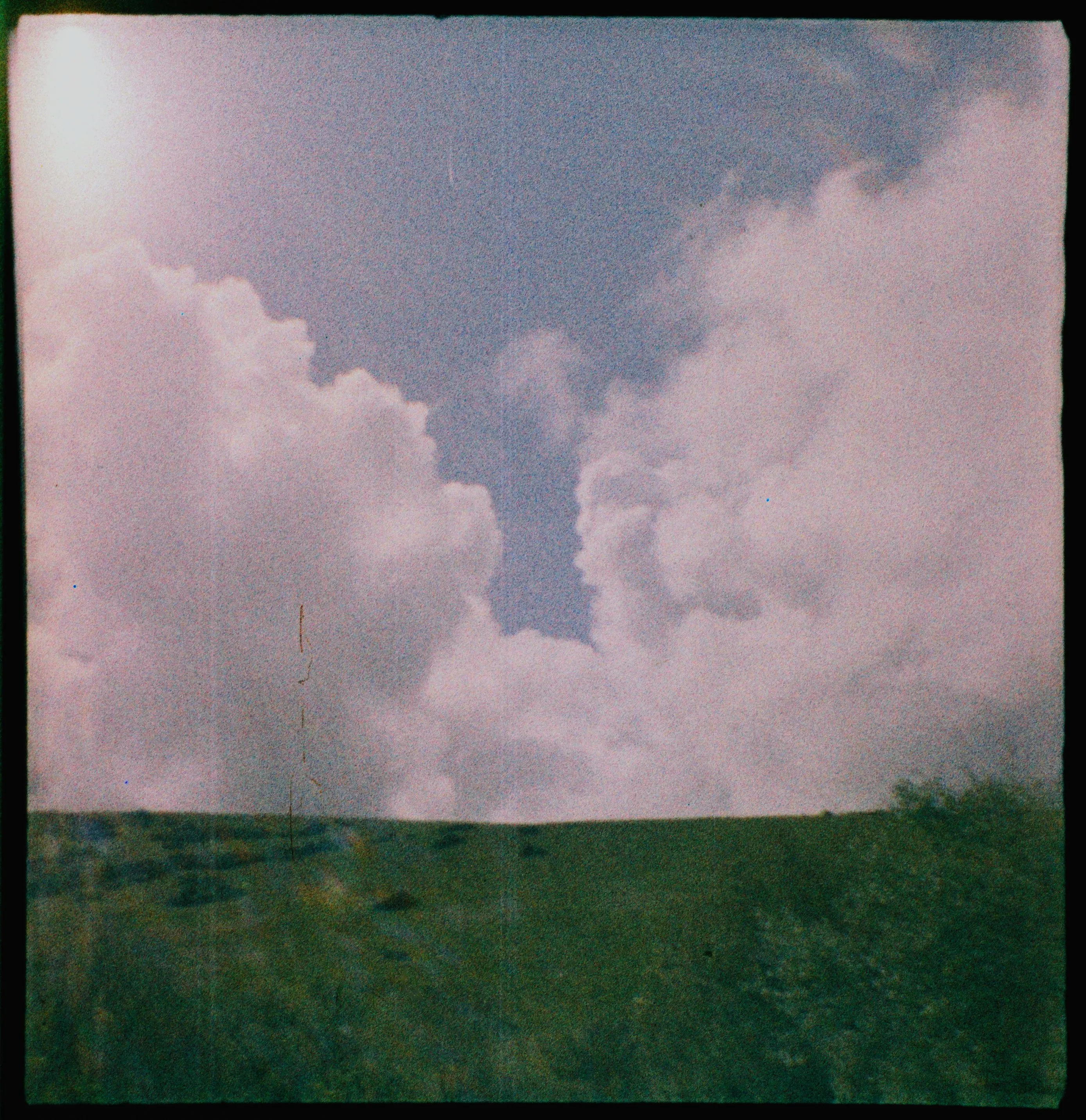 A photo of a landscape. The top two thirds are sun, blue sky and white fluffy clouds. The bottom third is bright green grass. It's almost unnaturally neat.