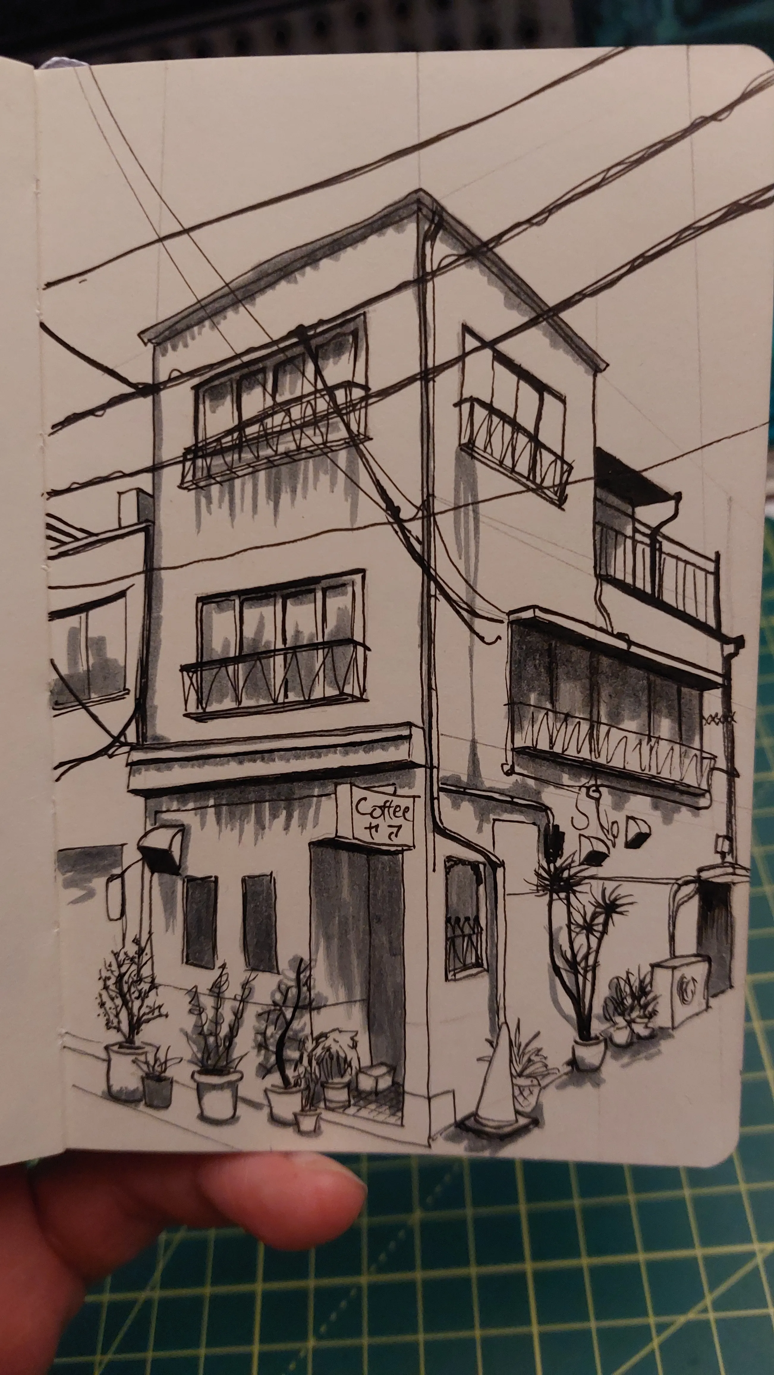 A Japanese building on a corner. A sign on the building says "Coffee". There are plants in pots all around the base of building. Above, cables criss-cross the street. The drawing is in black pen with shading in a grey felt pen that in hindsight is far too dark.
